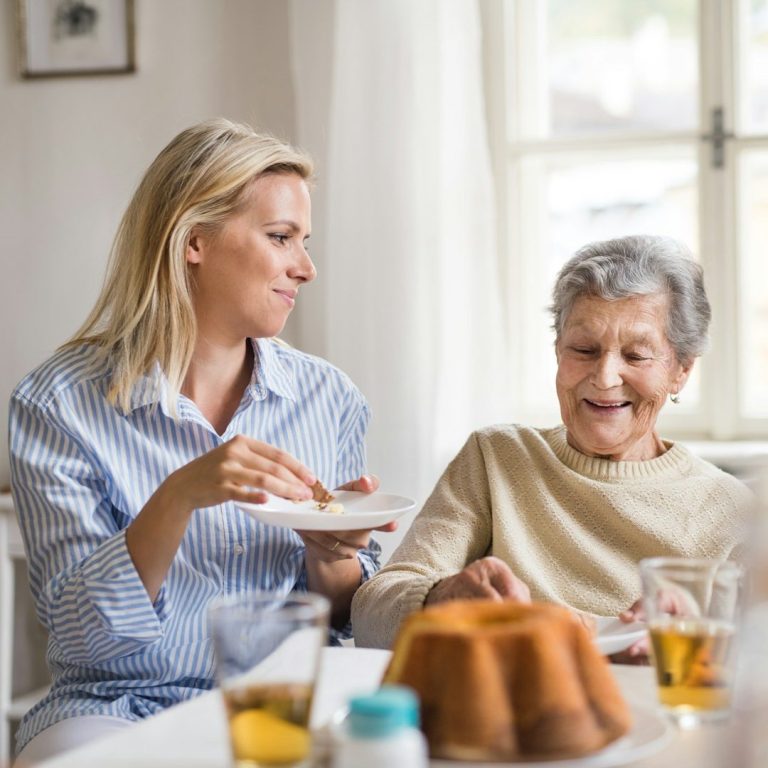 fröhliche alte Dame bei Kaffee und Kuchen mit ihrer erwachsenen Enkelin